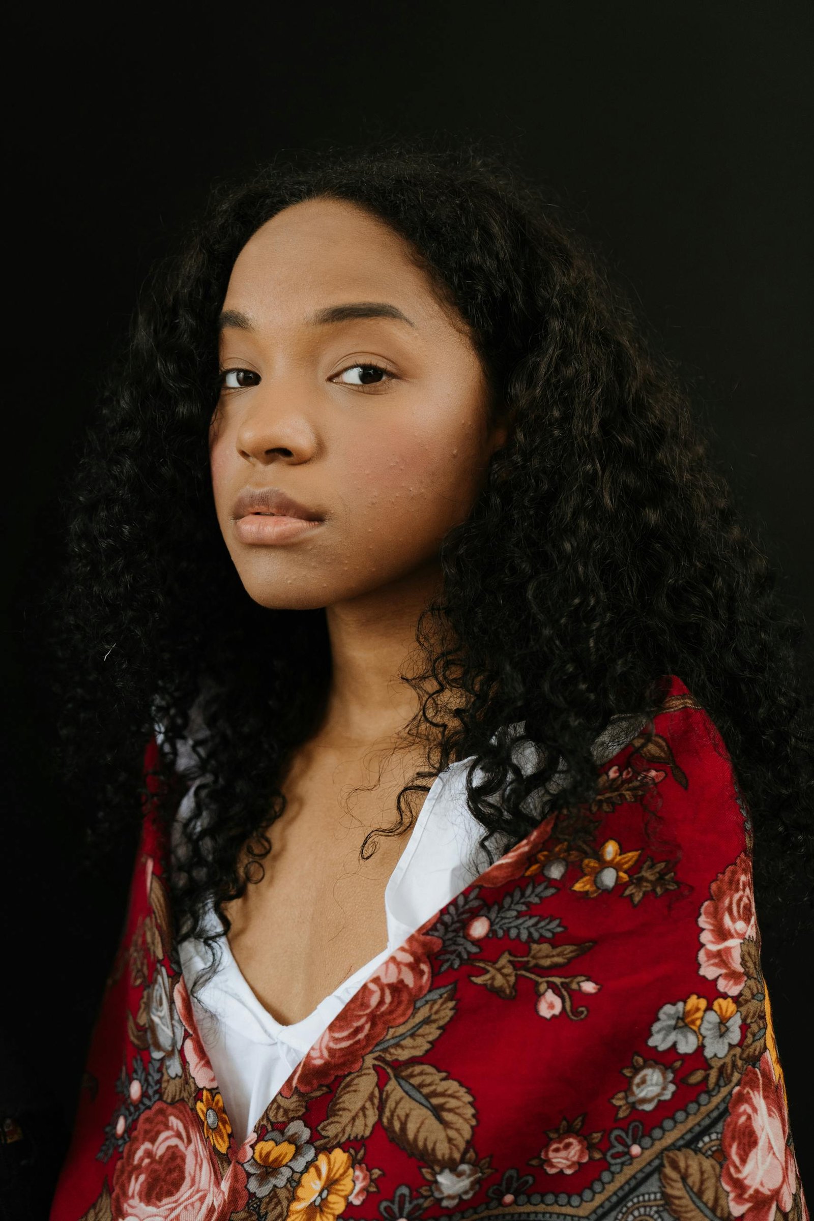 A beautiful woman draped in a floral shawl, posing against a black background.