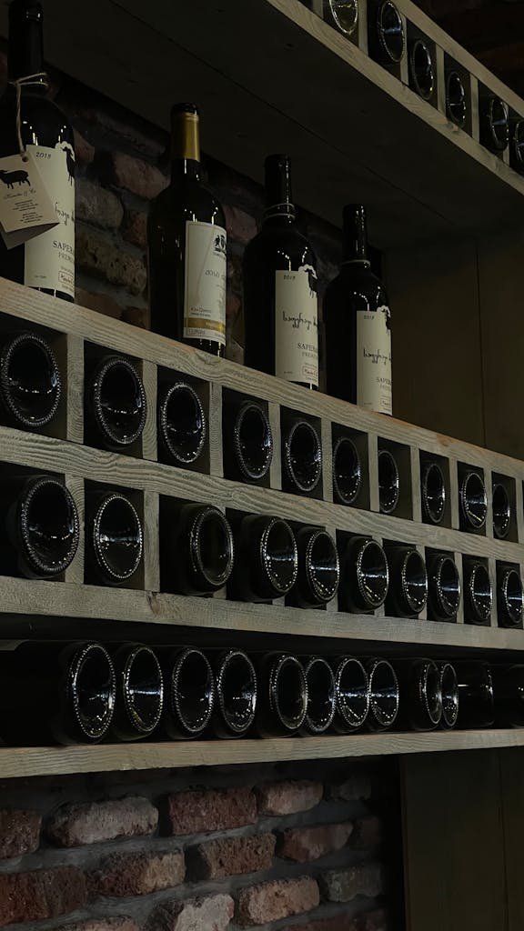 A vertical array of wine bottles on wood shelves set against a brick wall, ideal for wine enthusiasts.